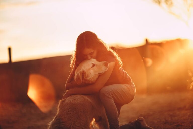 Eine Frau umarmt ihren Golden Retriever im warmen Licht der untergehenden Sonne.